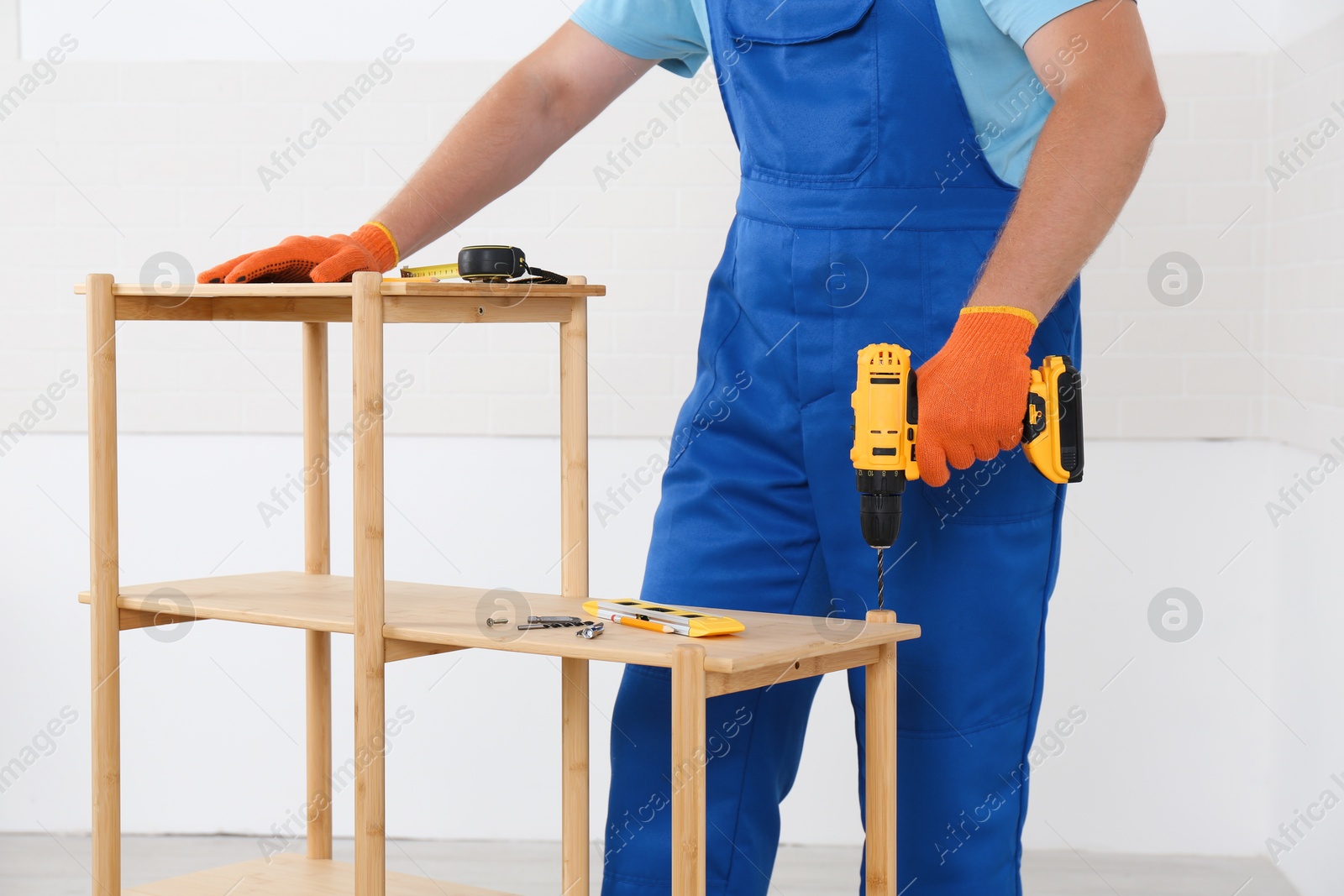 Photo of Worker with electric screwdriver assembling furniture indoors, closeup