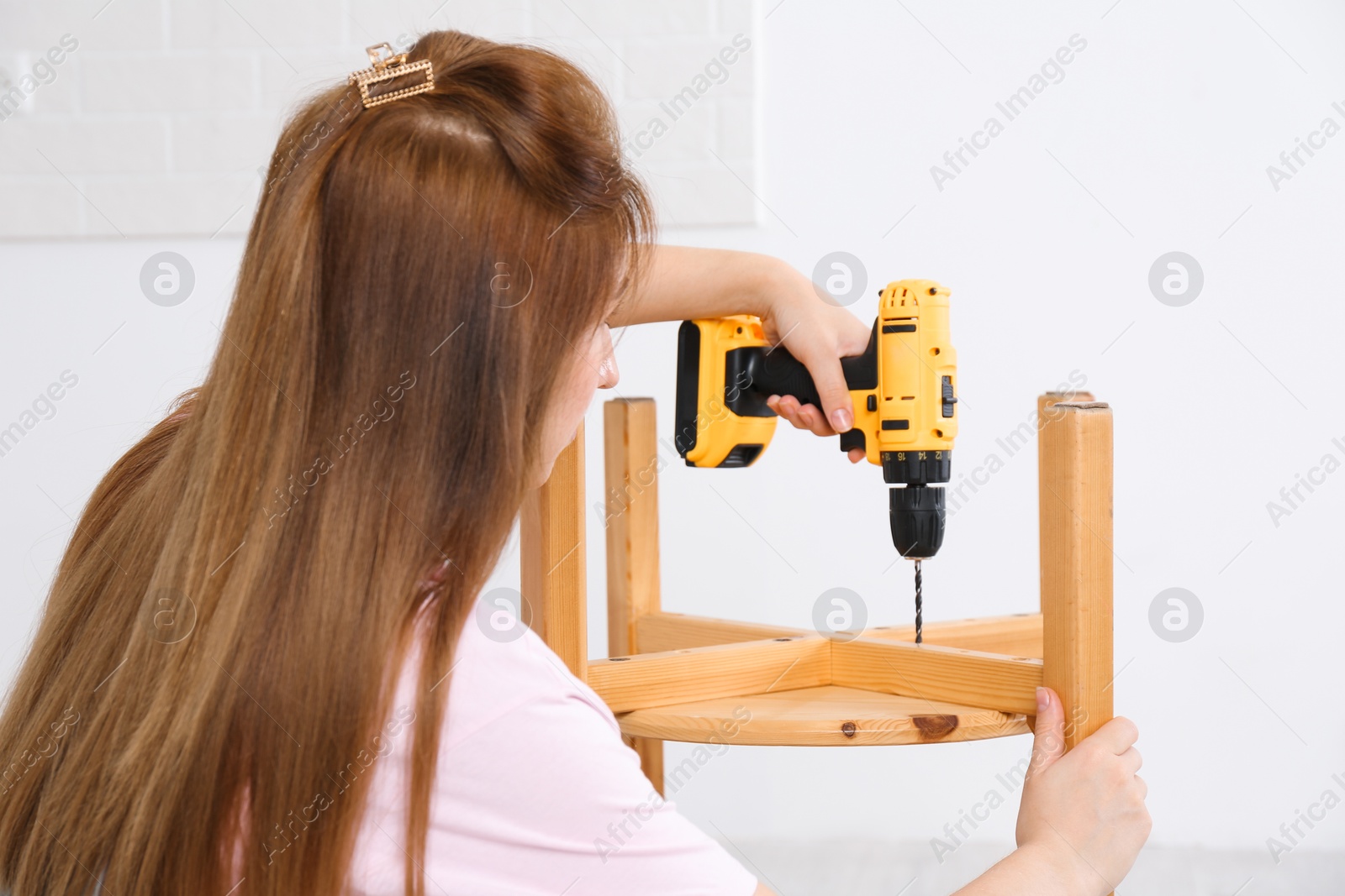 Photo of Woman with electric screwdriver assembling furniture indoors