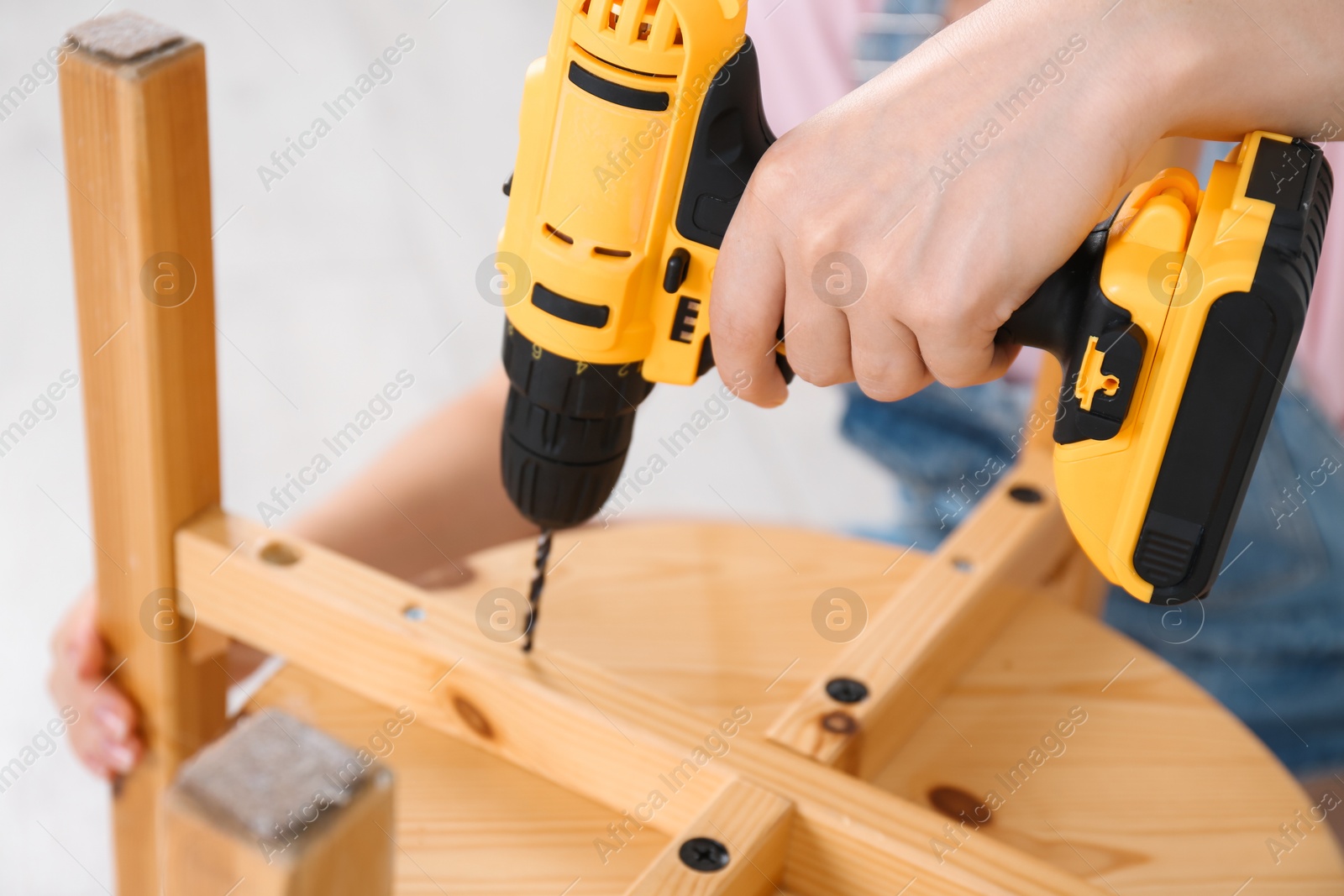 Photo of Woman with electric screwdriver assembling furniture indoors, closeup