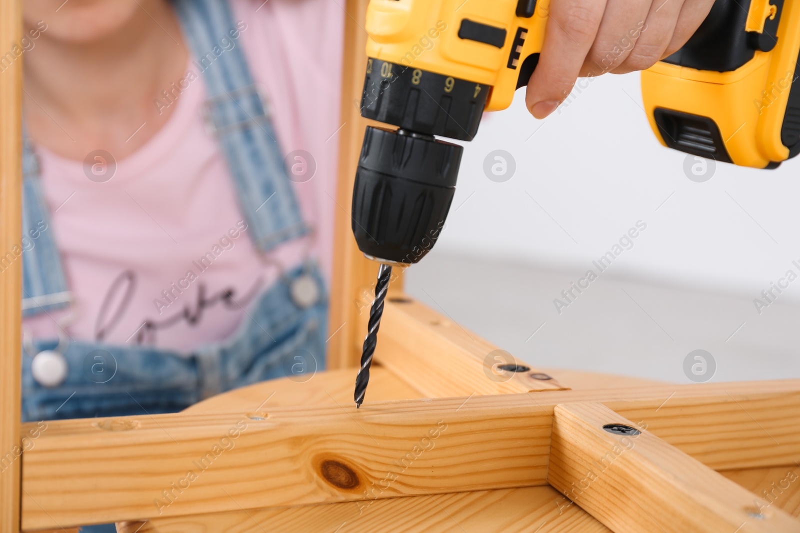 Photo of Woman with electric screwdriver assembling furniture indoors, closeup