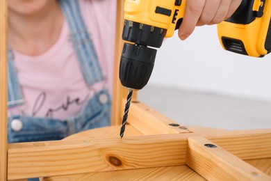 Woman with electric screwdriver assembling furniture indoors, closeup