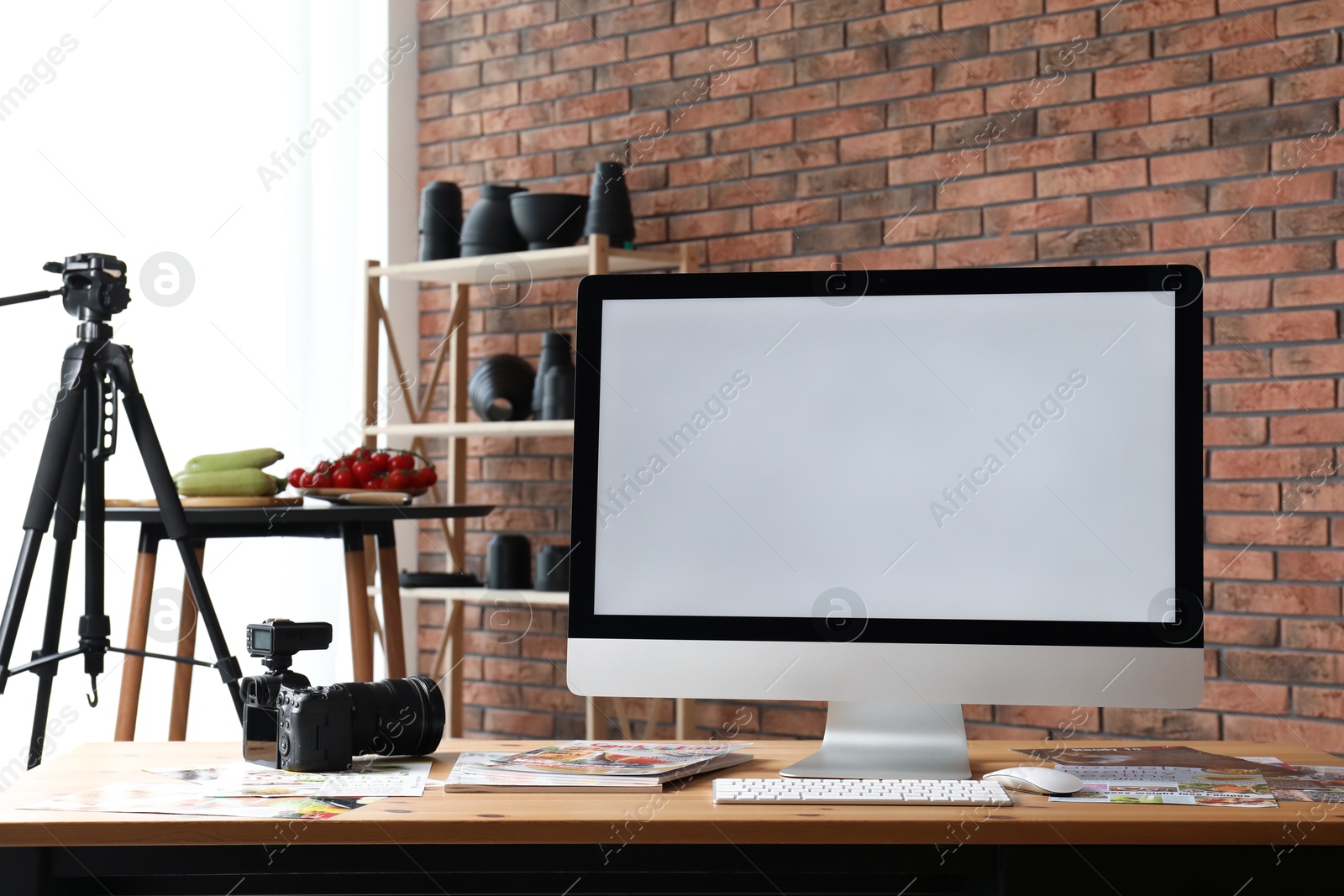 Photo of Computer, camera, magazines and vegetables on table in studio. Food photography