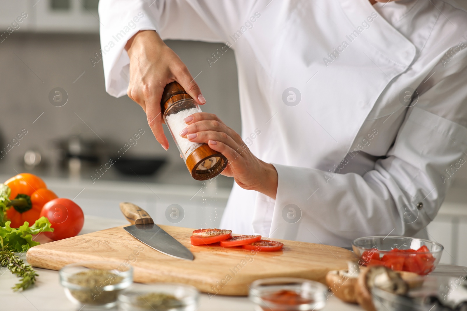 Photo of Professional chef seasoning tomatoes at table in kitchen, closeup