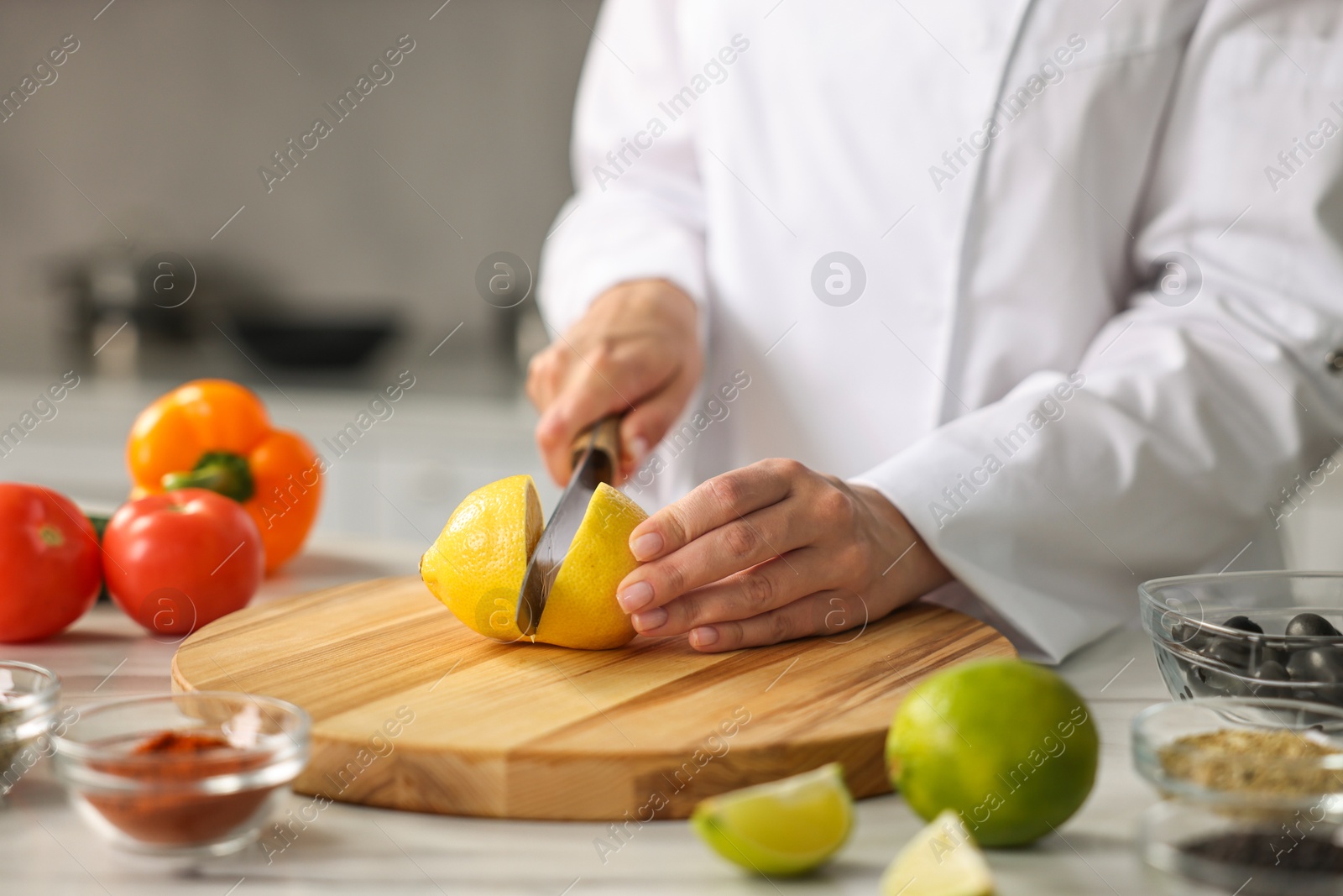 Photo of Professional chef cutting lemon at table in kitchen, closeup