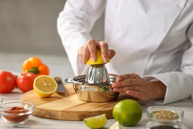 Woman squeezing juice out of lemon at table in kitchen, closeup