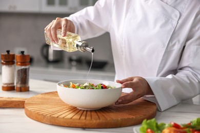 Photo of Professional chef pouring oil onto delicious salad at table in kitchen, closeup