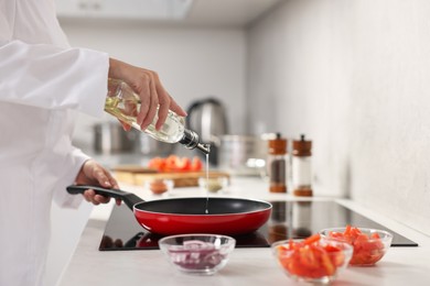 Photo of Professional chef pouring oil into frying pan in kitchen, closeup