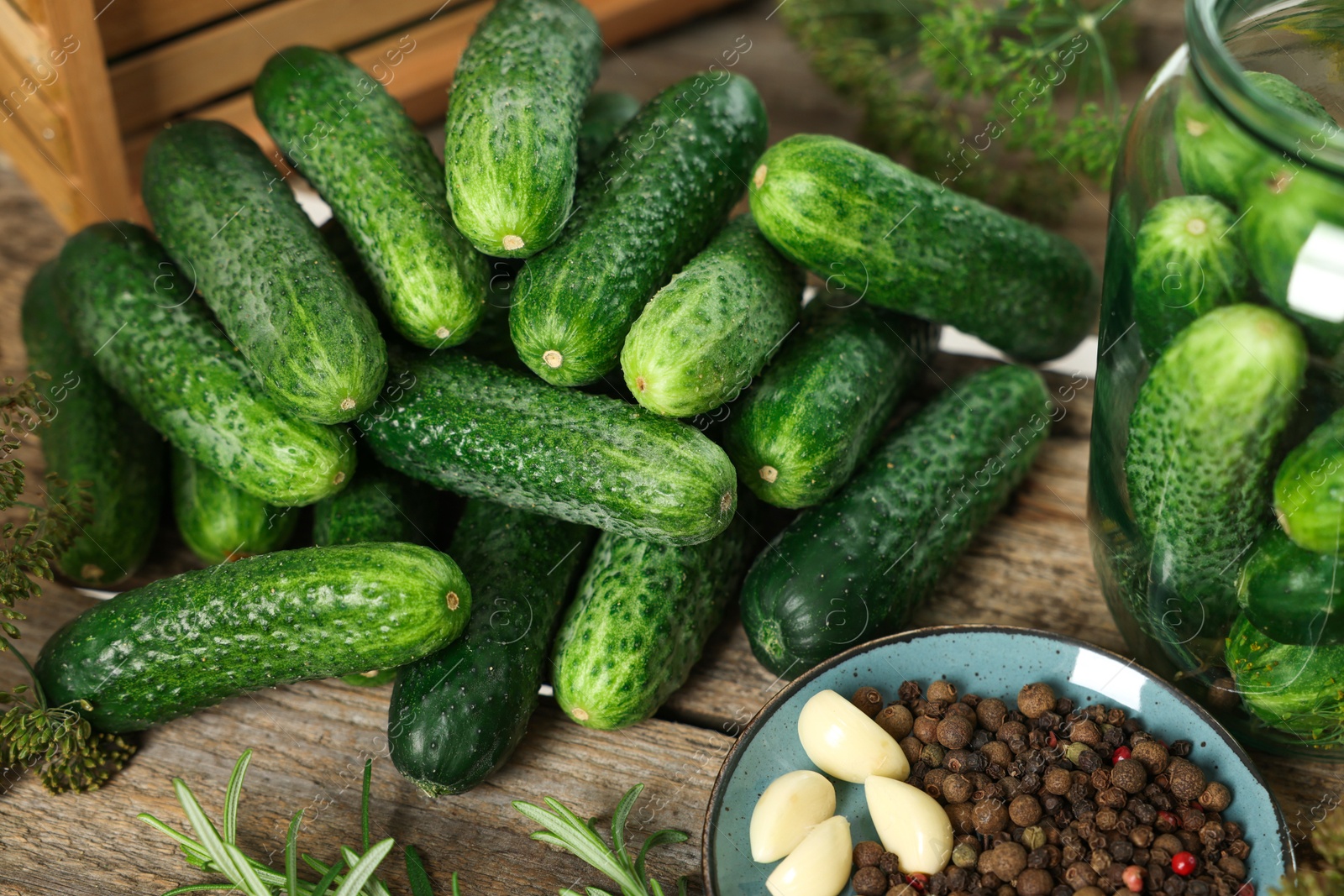 Photo of Pile of fresh cucumbers and spices on wooden table, closeup. Preparation for pickling