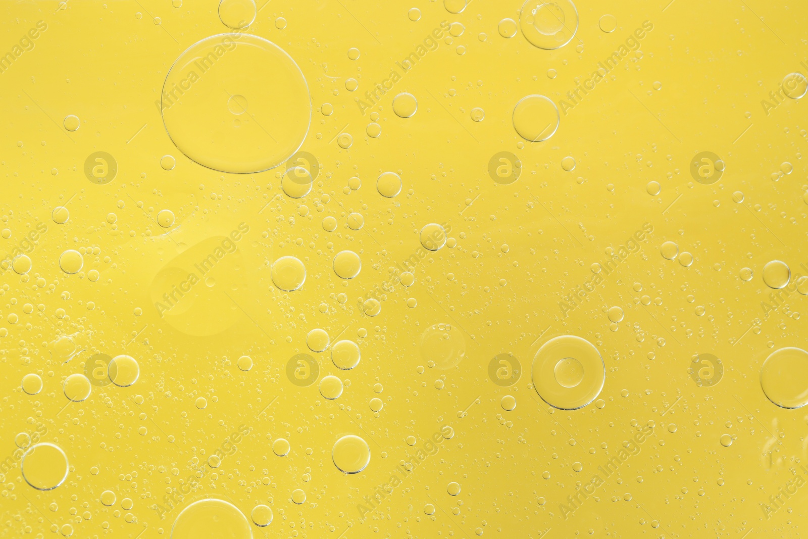 Photo of Essential oil bubbles on yellow background, macro view. Cosmetic product