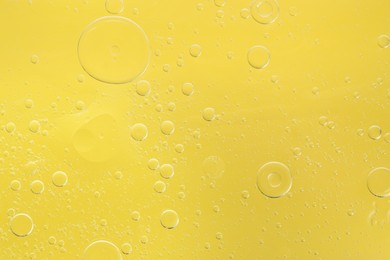 Photo of Essential oil bubbles on yellow background, macro view. Cosmetic product