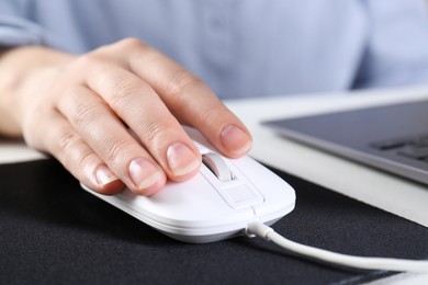 Photo of Woman using computer mouse while working with laptop at white table, closeup