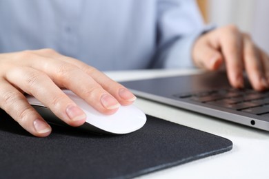 Photo of Woman using computer mouse while working with laptop at white table, closeup