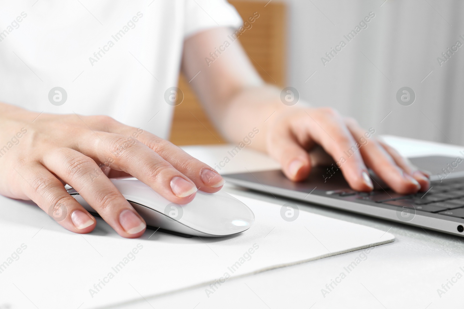 Photo of Woman using computer mouse while working with laptop at white table, closeup