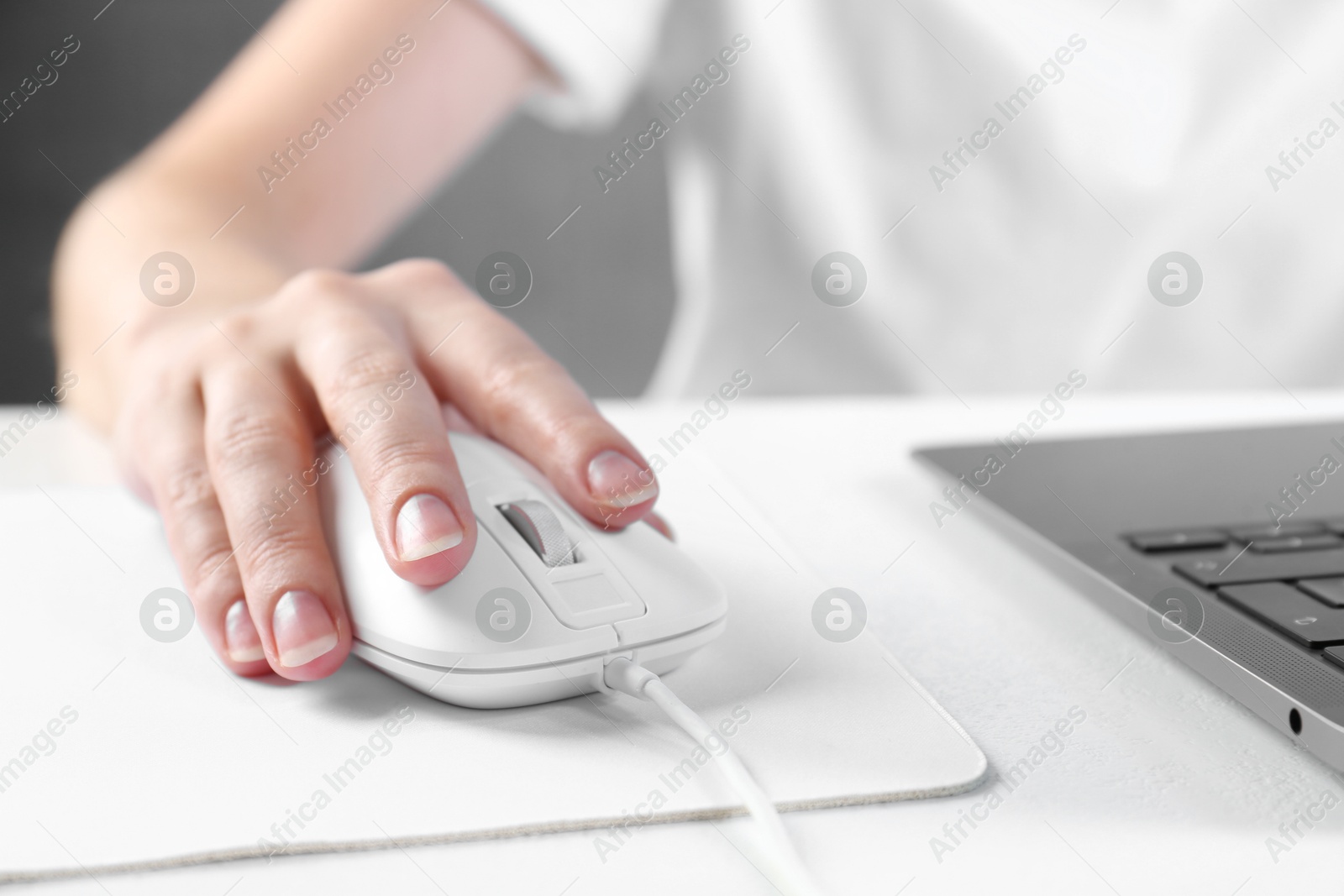 Photo of Woman using computer mouse while working with laptop at white table, closeup