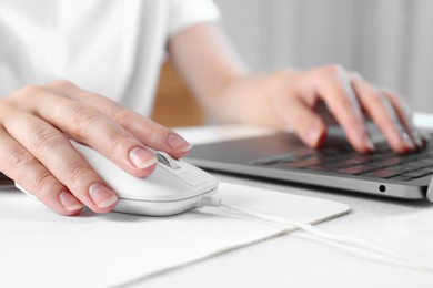 Photo of Woman using computer mouse while working with laptop at white table, closeup