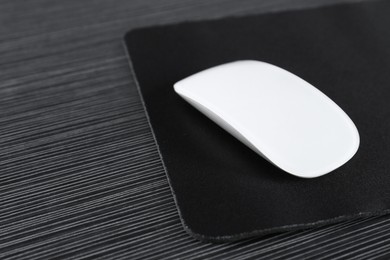 Photo of White computer mouse with mousepad on black wooden table