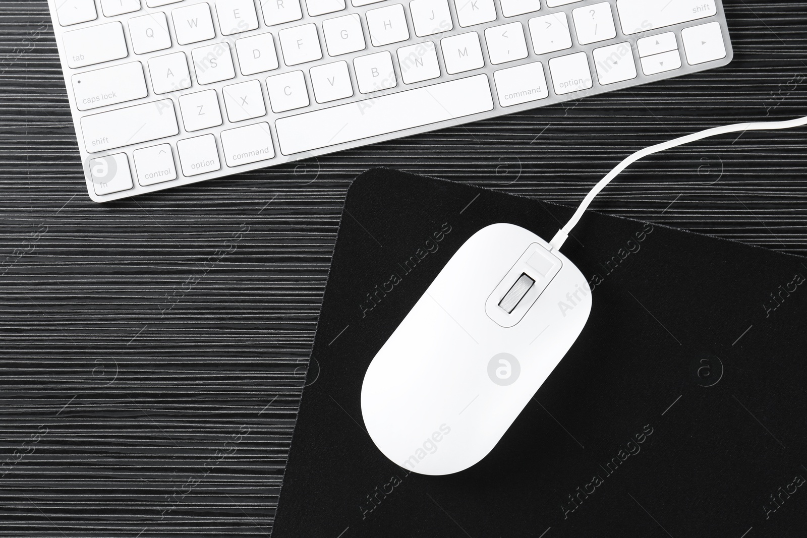 Photo of White computer mouse with mousepad and keyboard on black wooden table, flat lay