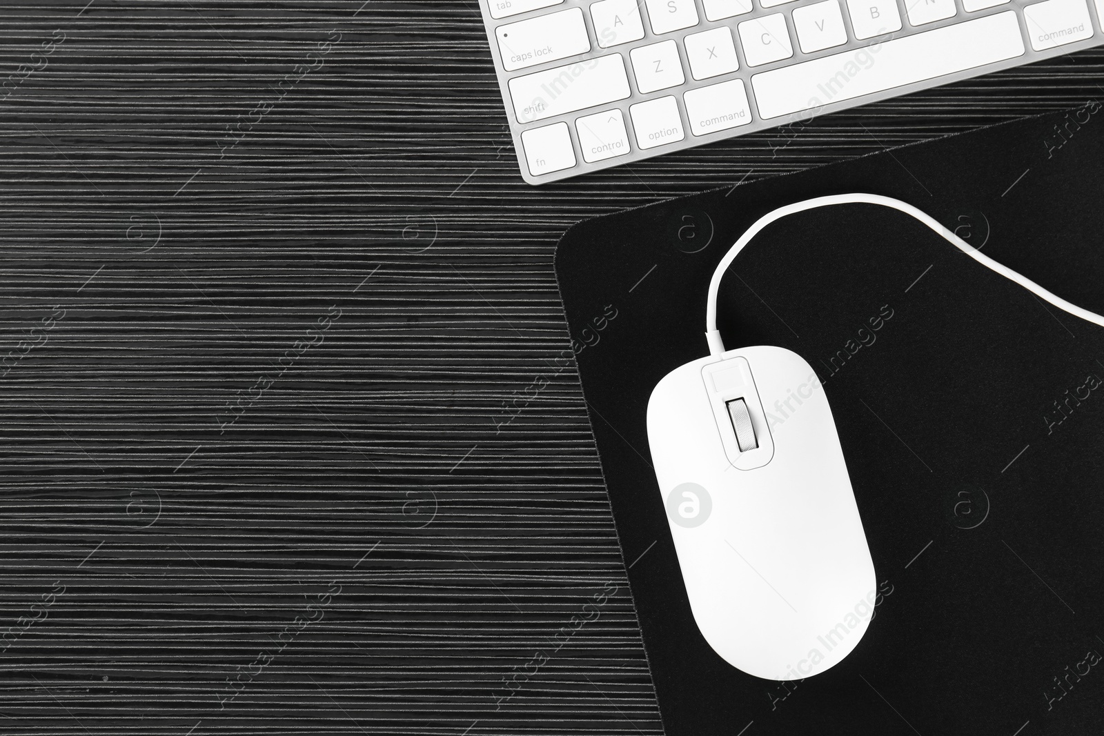 Photo of White computer mouse with mousepad and keyboard on black wooden table, flat lay