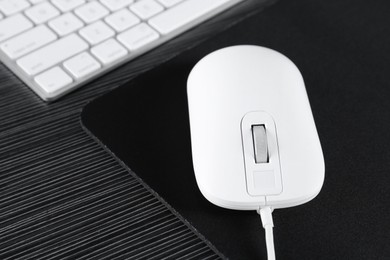 Photo of White computer mouse with mousepad and keyboard on black wooden table, closeup