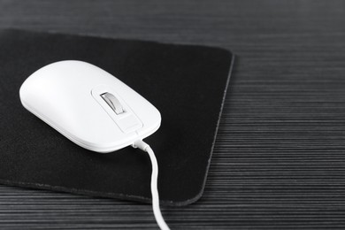 Photo of White computer mouse with mousepad on black wooden table