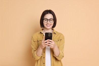 Smiling woman with smartphone on beige background