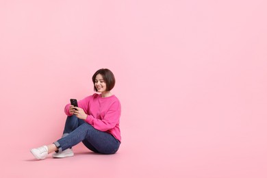 Photo of Smiling woman with smartphone sitting on pink background. Space for text