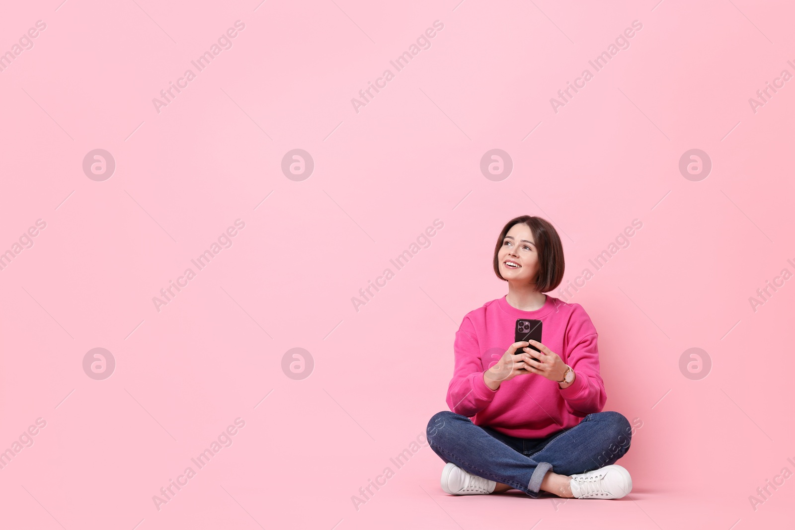 Photo of Smiling woman with smartphone sitting on pink background. Space for text