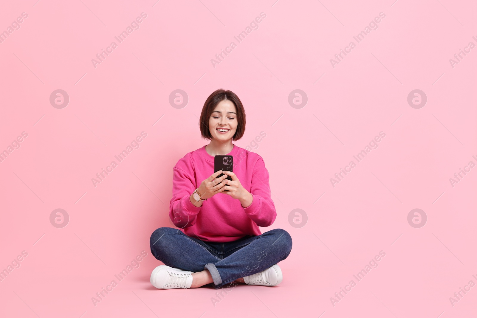 Photo of Smiling woman with smartphone sitting on pink background