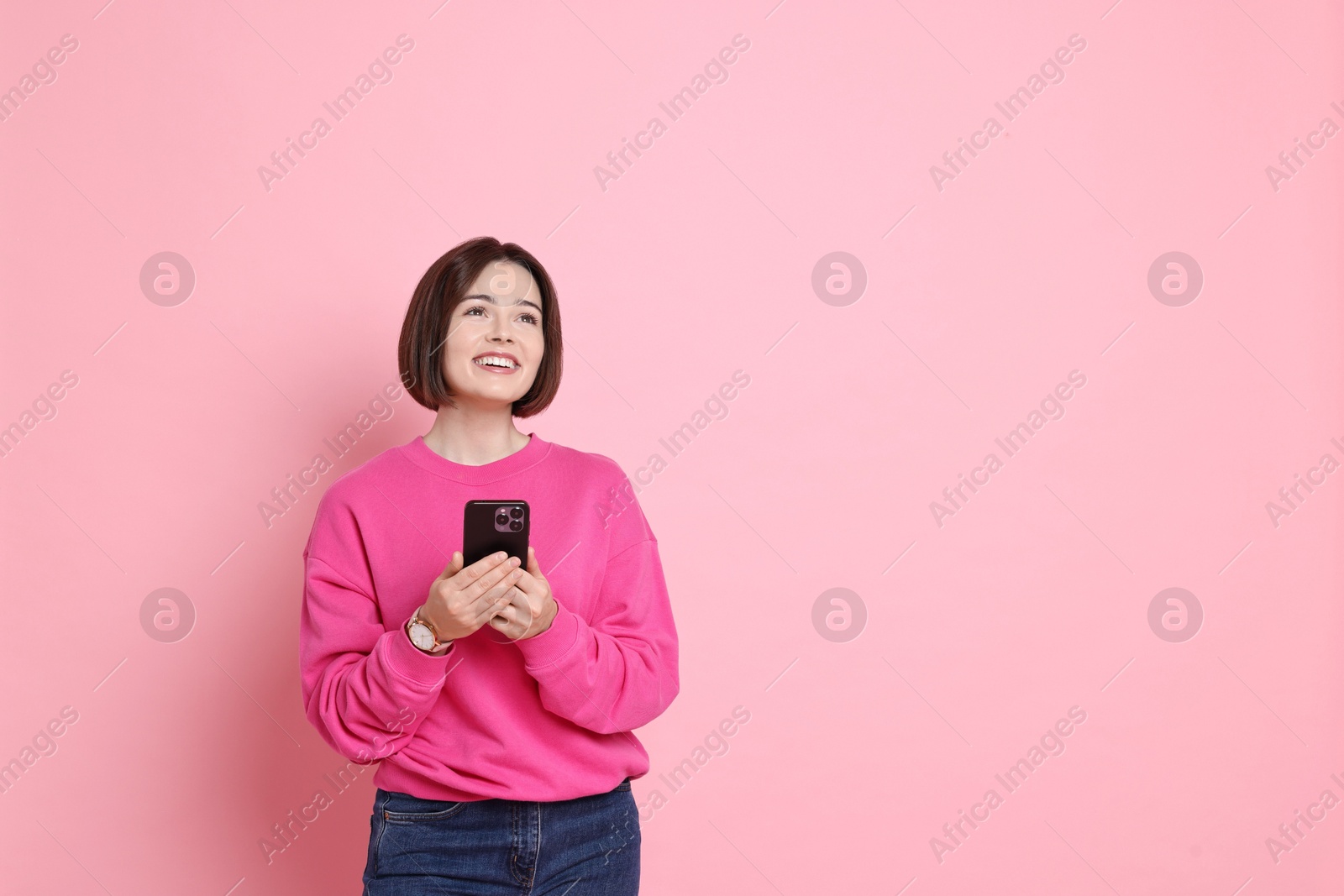 Photo of Smiling woman with smartphone on pink background. Space for text