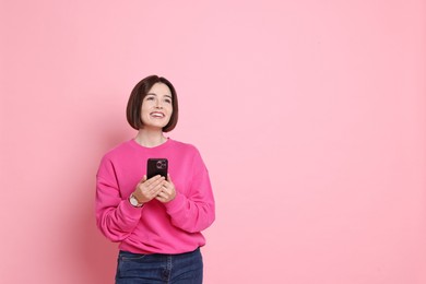 Photo of Smiling woman with smartphone on pink background. Space for text