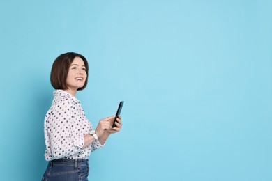 Photo of Smiling woman with smartphone on light blue background. Space for text