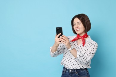 Smiling woman with smartphone on light blue background. Space for text