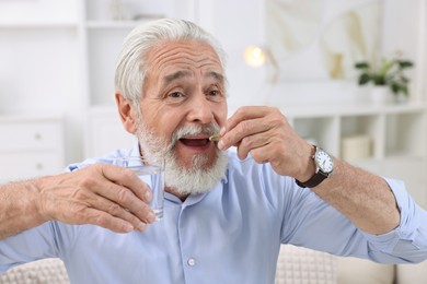 Photo of Senior man with glass of water taking pill at home