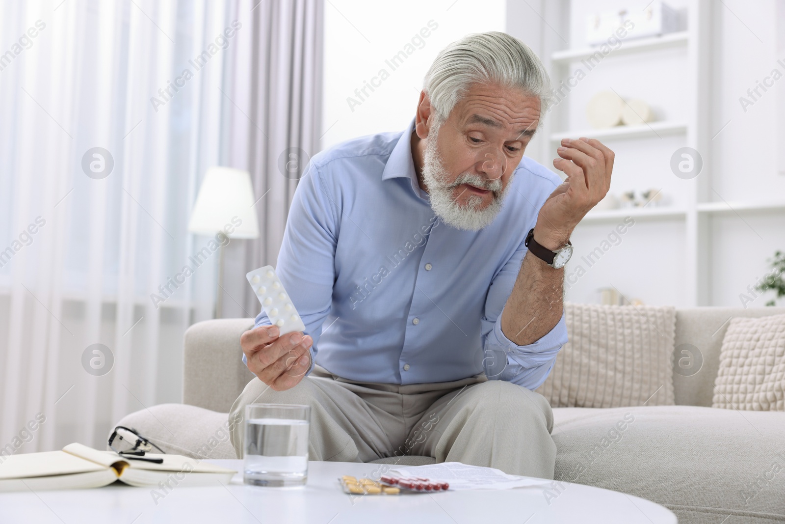 Photo of Senior man with pills on sofa at home