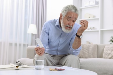 Senior man with pills on sofa at home