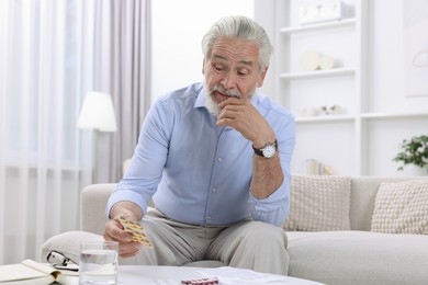 Senior man with pills on sofa at home