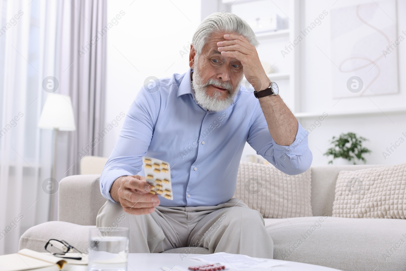 Photo of Senior man with pills on sofa at home