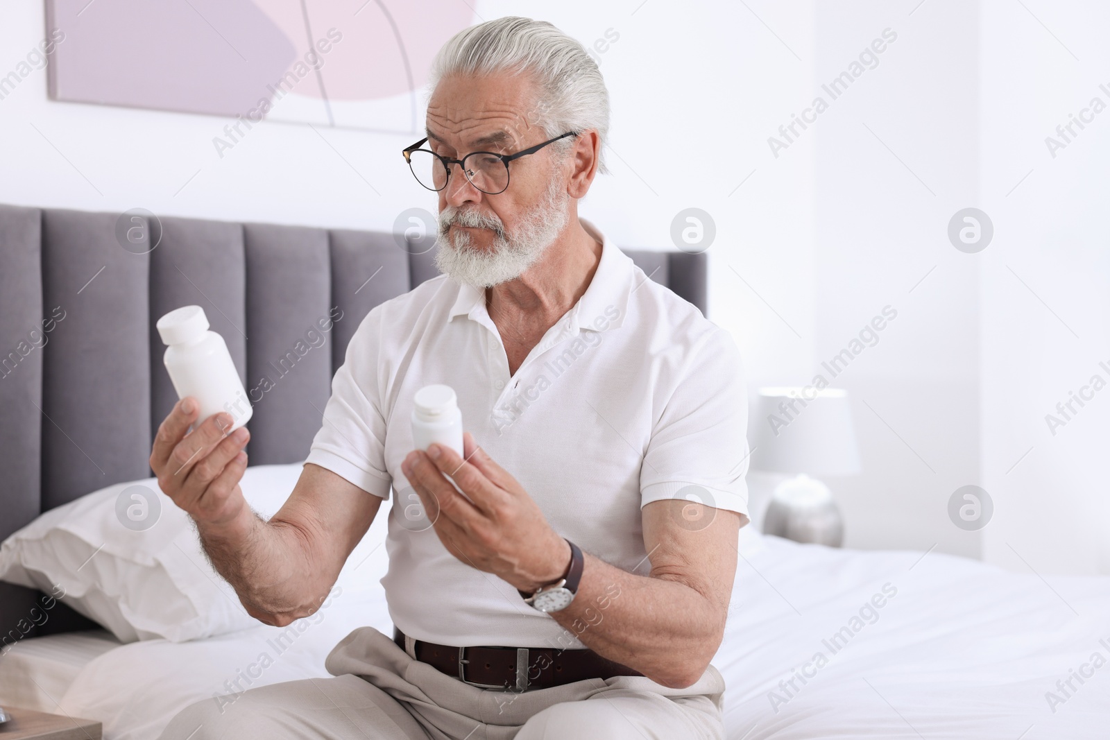 Photo of Senior man with bottles of pills on bed indoors, space for text