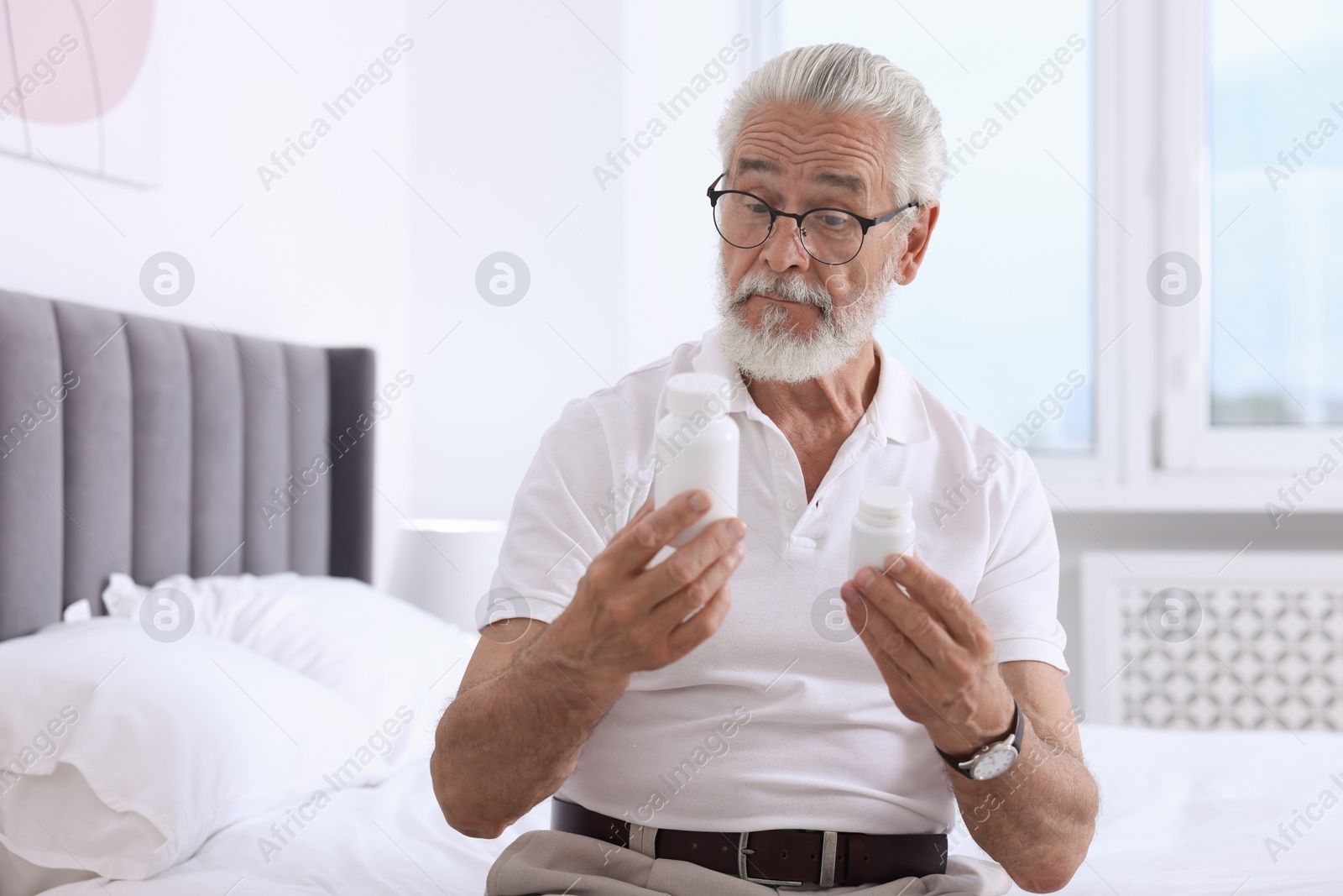 Photo of Senior man with bottles of pills on bed indoors