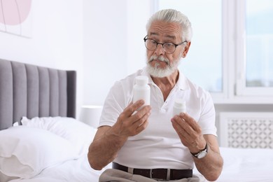 Senior man with bottles of pills on bed indoors