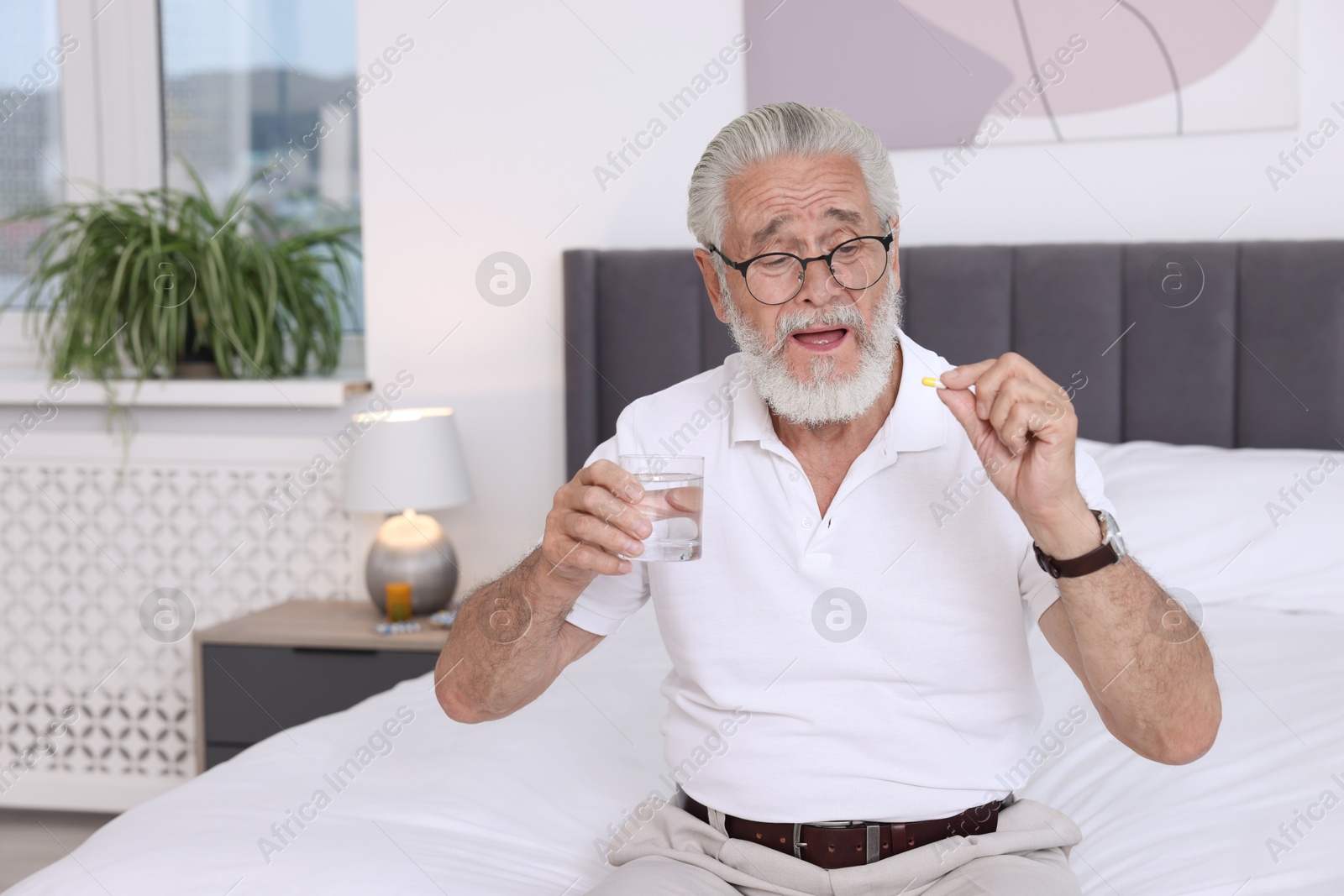 Photo of Senior man with glass of water and pill on bed at home