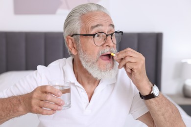 Senior man with glass of water taking pill at home