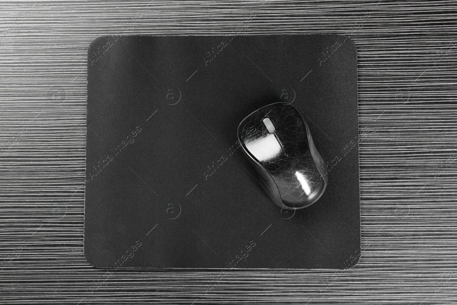 Photo of Computer mouse with mousepad on black wooden table, top view