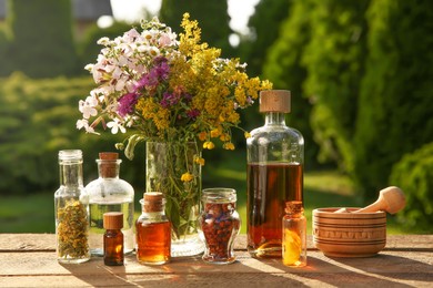 Photo of Different tinctures in bottles, ingredients, mortar and pestle on wooden table outdoors