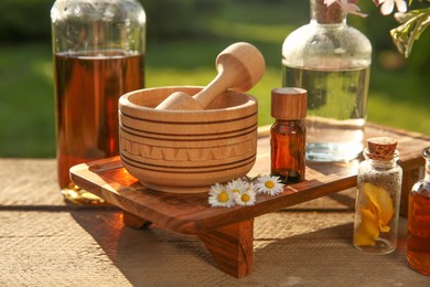 Photo of Different tinctures in bottles, ingredients, mortar and pestle on wooden table outdoors