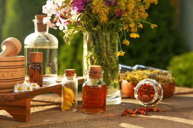 Photo of Different tinctures in bottles, ingredients, mortar and pestle on wooden table outdoors