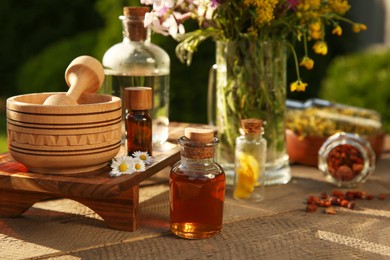 Photo of Tincture in bottles, different ingredients, mortar and pestle on wooden table outdoors