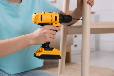 Photo of Woman with electric screwdriver assembling furniture in room, closeup