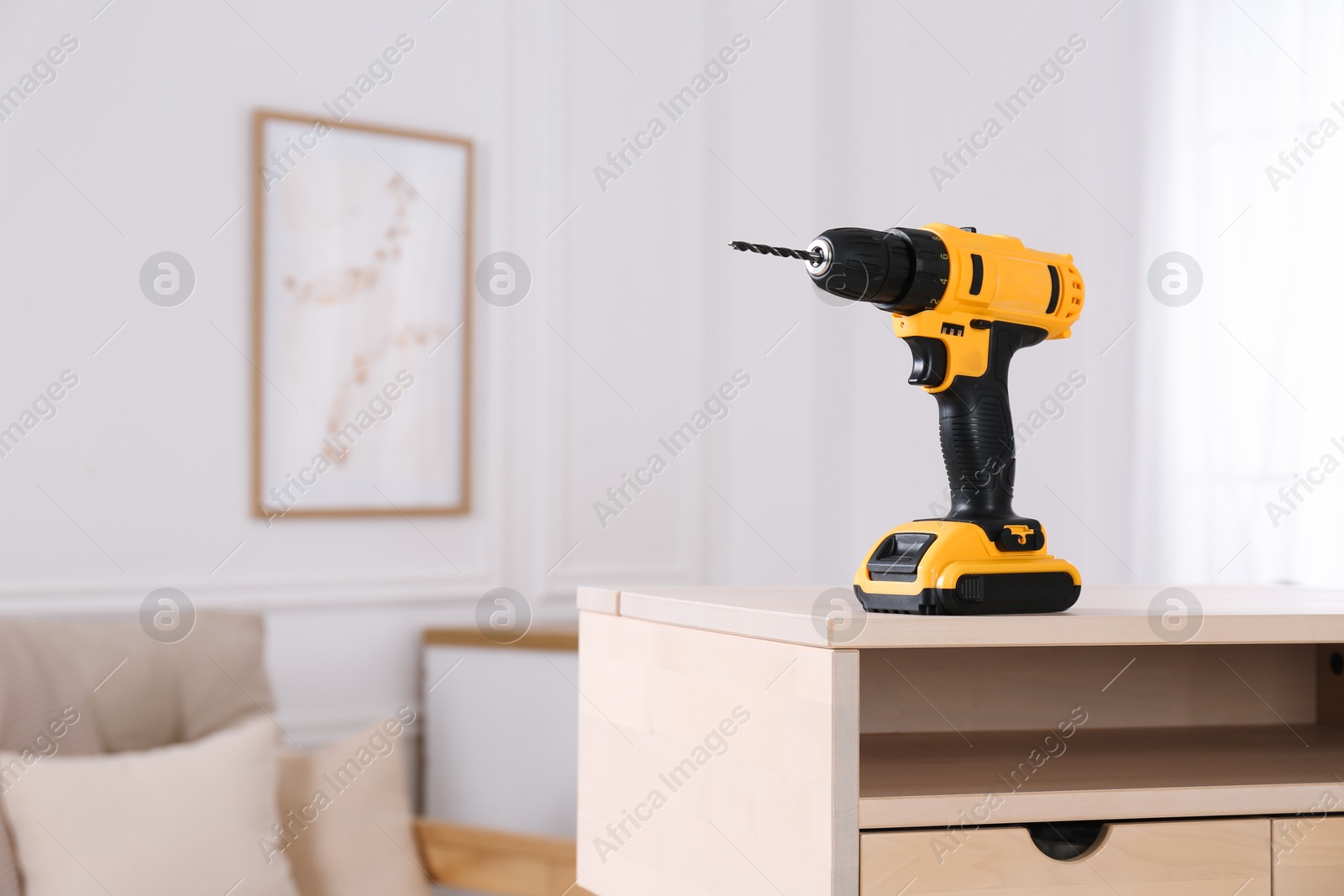 Photo of Cordless electric screwdriver on wooden table at home. Space for text