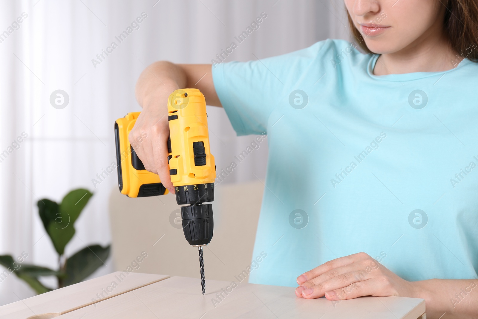 Photo of Woman with electric screwdriver assembling furniture at home, closeup